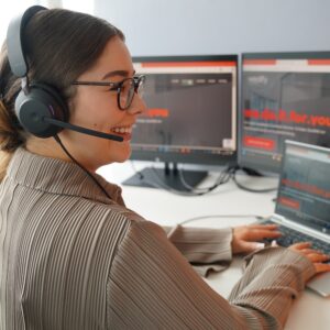 eine Frau mit Kopfhörern, die vor einem Computerbildschirm sitzt und lächelt