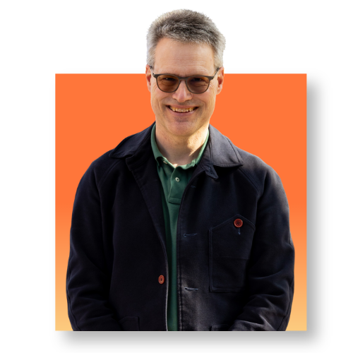 eine Mann im Portrait mit kurzen, grauen Haaren und einem schwarzen Shirt. vor einem quadratischen Hintergrund in Orange