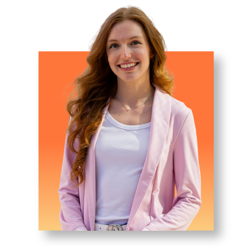 eine Frau im Portrait mit langen, orangenen Haaren und einem rosa Blazer und weißem Shirt. vor einem quadratischen Hintergrund in Orange