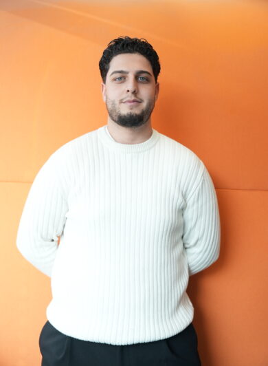 ein Mann im Portrait mit weißem Pulli und kurzen schwarzen Haaren