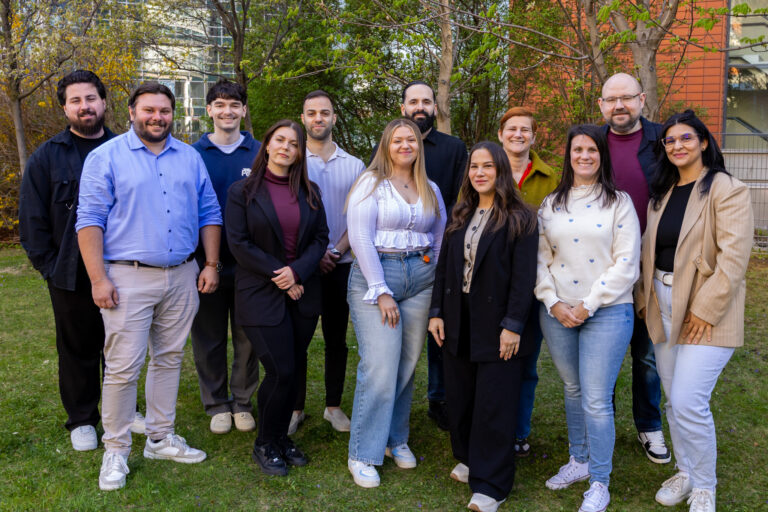 Ein Team mit 12 Mitgliedern auf einem Gruppenfoto. Sie stehen im Freien und lachen alle