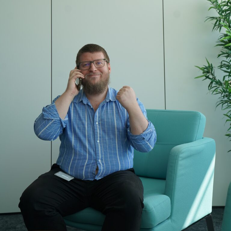 ein Mann sitzt in einem Couch-Sessel und telefoniert. Er ballt vor Freude eine Siegesfaust und lacht