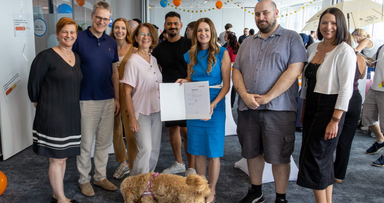 Ein Gruppenfoto von 6 erwachsenen Personen in einem Party-geschmückten Raum