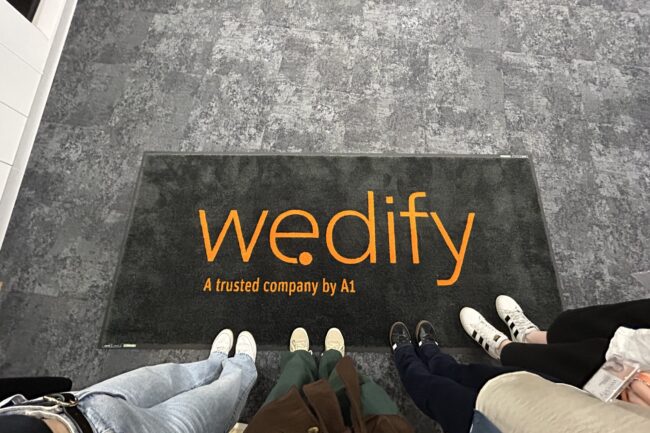 Blick von oben auf 3 Personen und eine Fußmatte, auf der we.dify steht