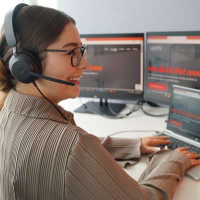 eine Frau mit Kopfhörern, die vor einem Computerbildschirm sitzt und lächelt